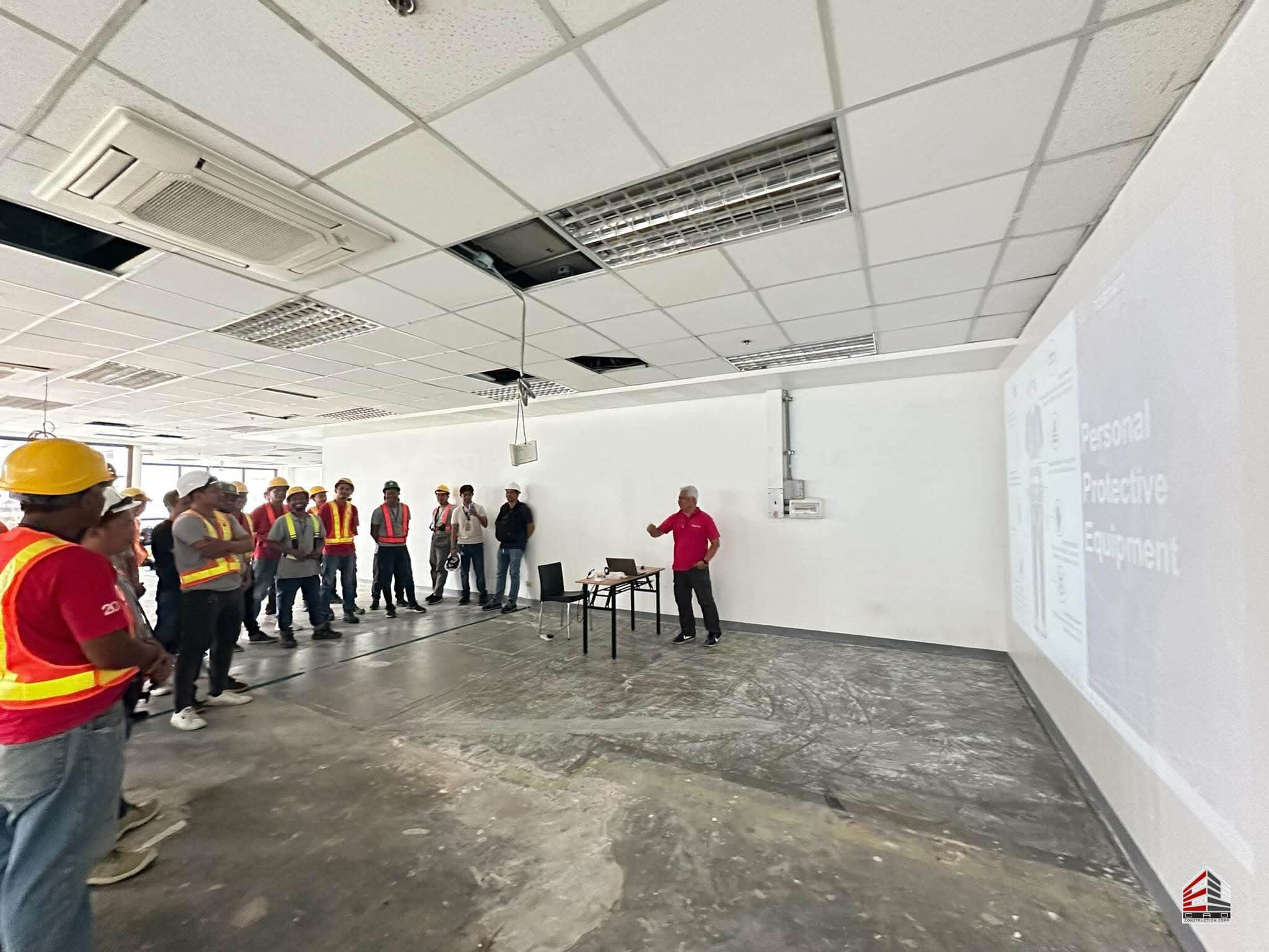 The Elcad project team standing in a gutted office space during a PPE presentation, highlighting the importance of safety protocols in the early stages of a fit-out.