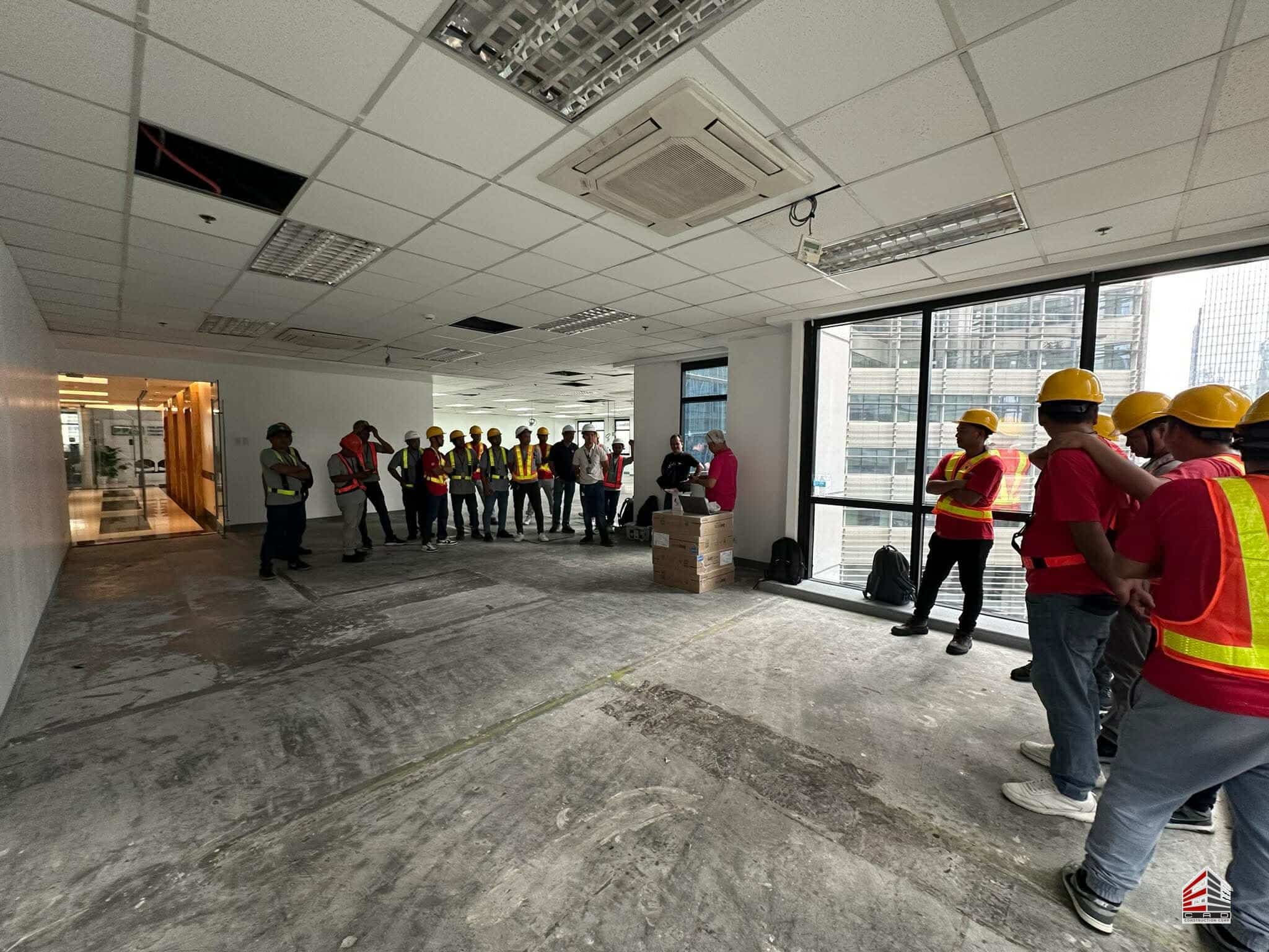 Workers gathered near large windows in an office under construction, looking toward a safety presentation at the 600sqm BGC project site.
