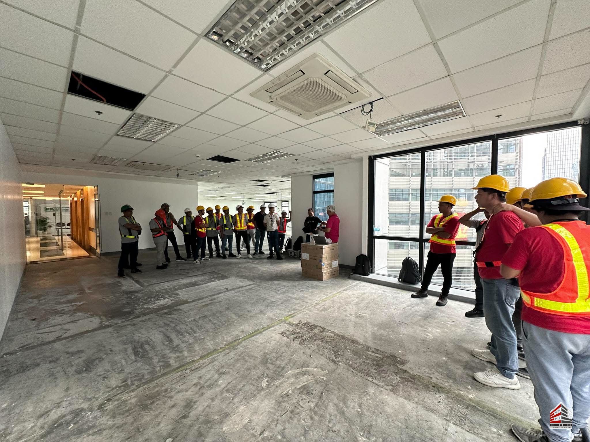 A wide view of the office interior showing the concrete flooring and exposed ceiling during a team safety meeting.